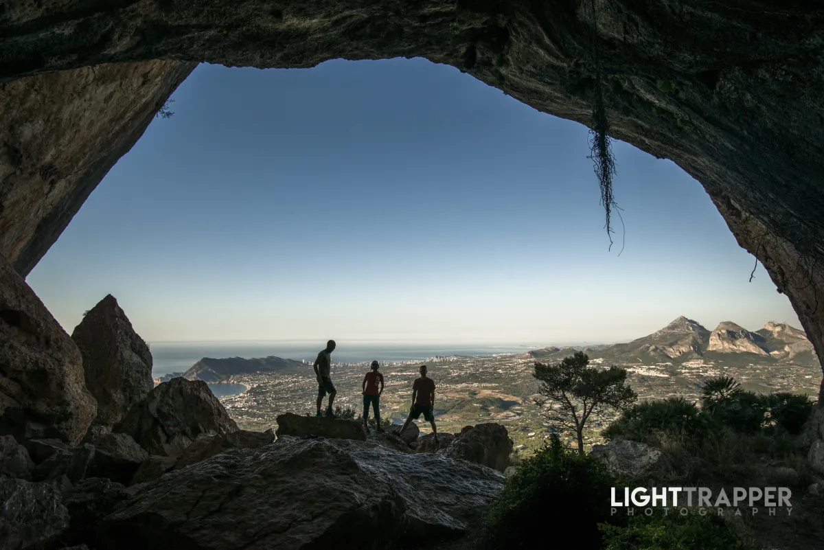 Three climbers hanging out on the coast-facing side of Forat, with Benidorm and Puig Campana in the background