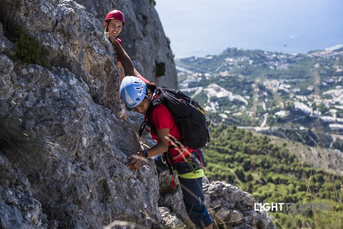 A concentrated climber making a tricky, exposed move, with another climber watching form behind