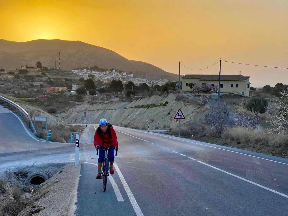 Wendy riding a bike uphill, beautiful sunrise in the background