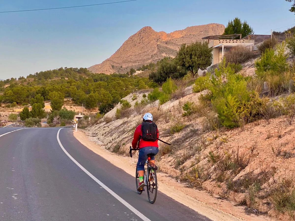 Wendy riding a bike uphill with El Realet Ridge in the background