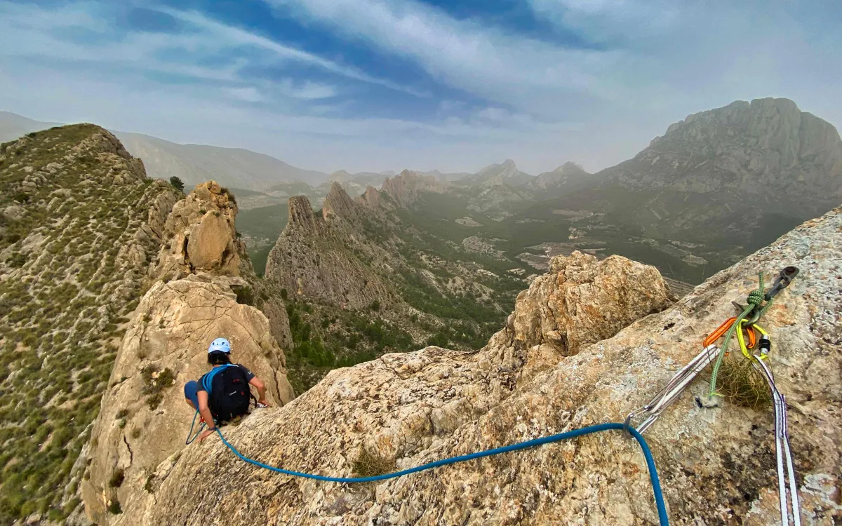 Climber sitting on the edge of a rock secured by a rope going through an anchor
