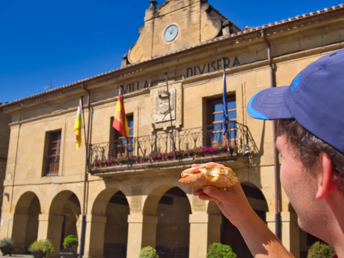 A man holding a sandwich in front of him with town hall as backdrop