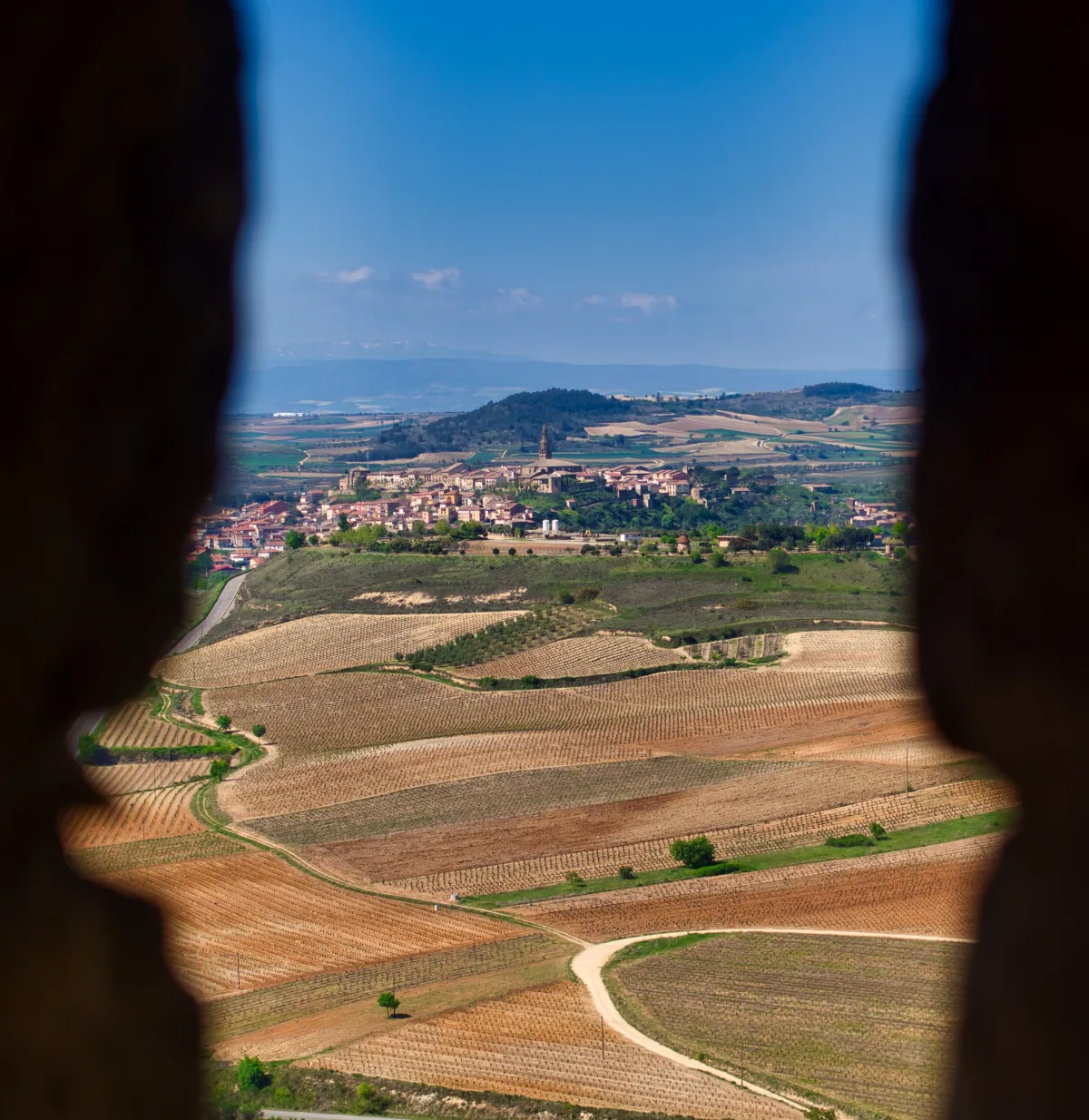 A small town on a hill and vineyards seen from a narrow opening in a castle wall