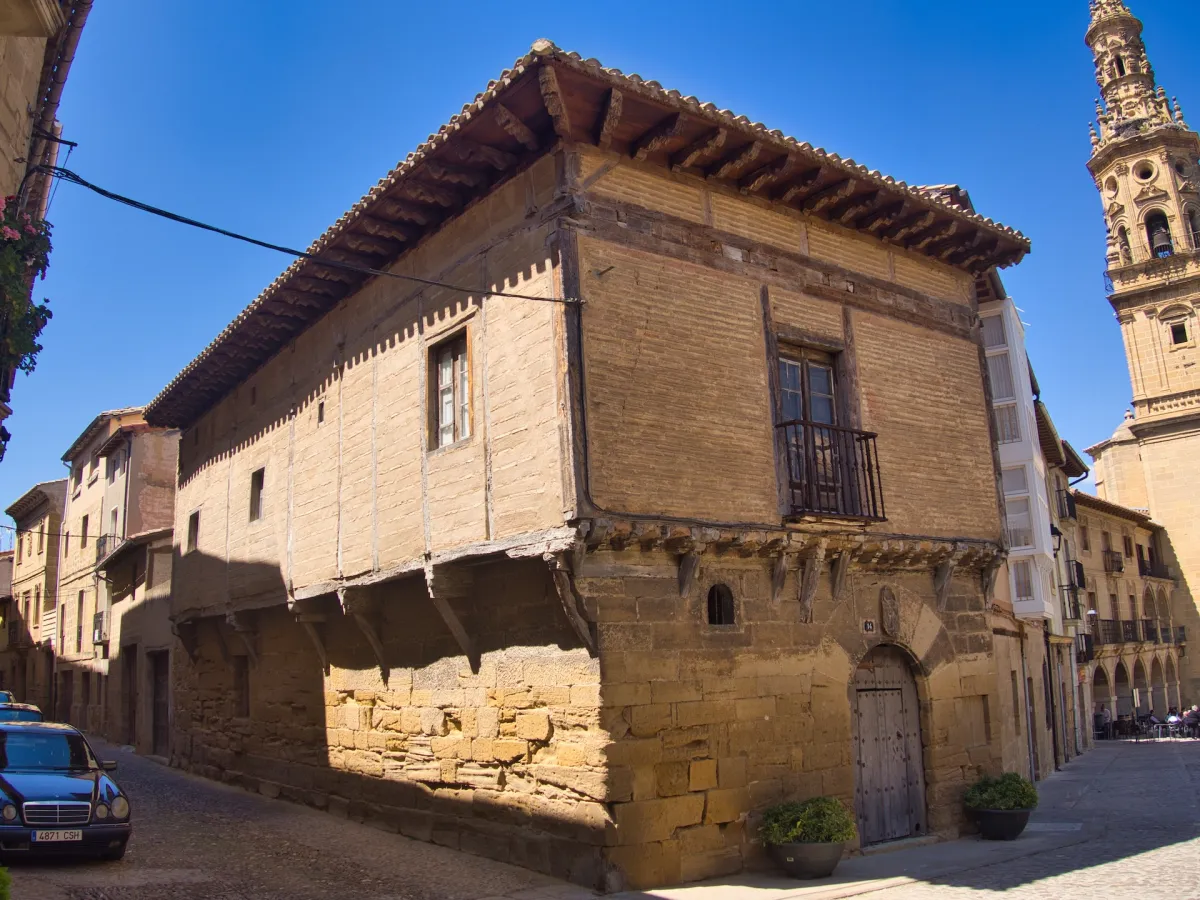 An old stone and brick building with wooden beams, church tower in the background