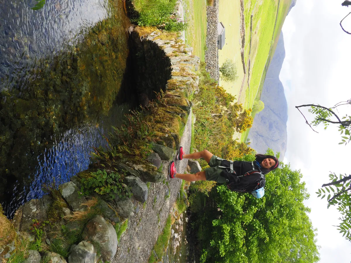 A climber on an antique bridge made out of stone, over Mosedale Beck